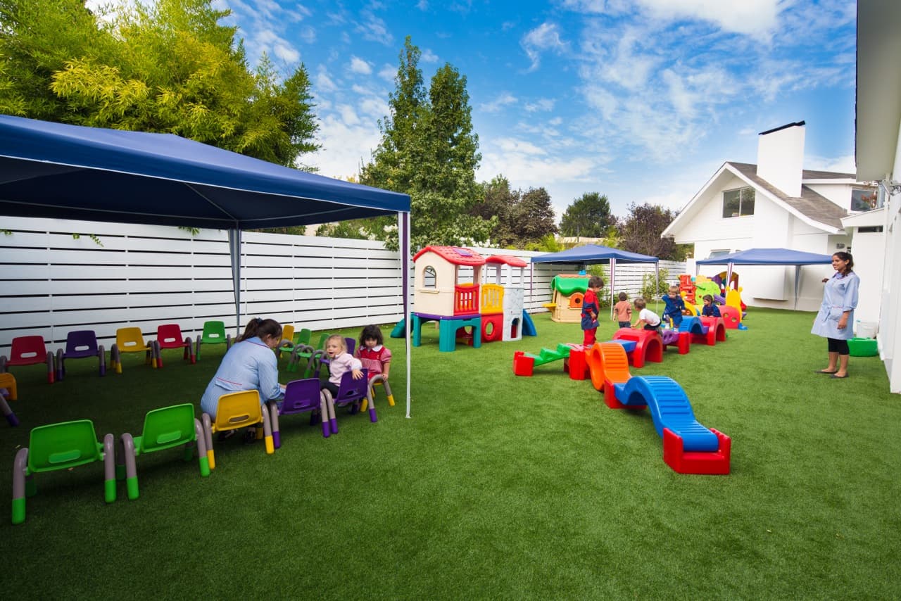 Niños y educadora disfrutando el patio exterior con cielo azul, Marco Polo Las Condes