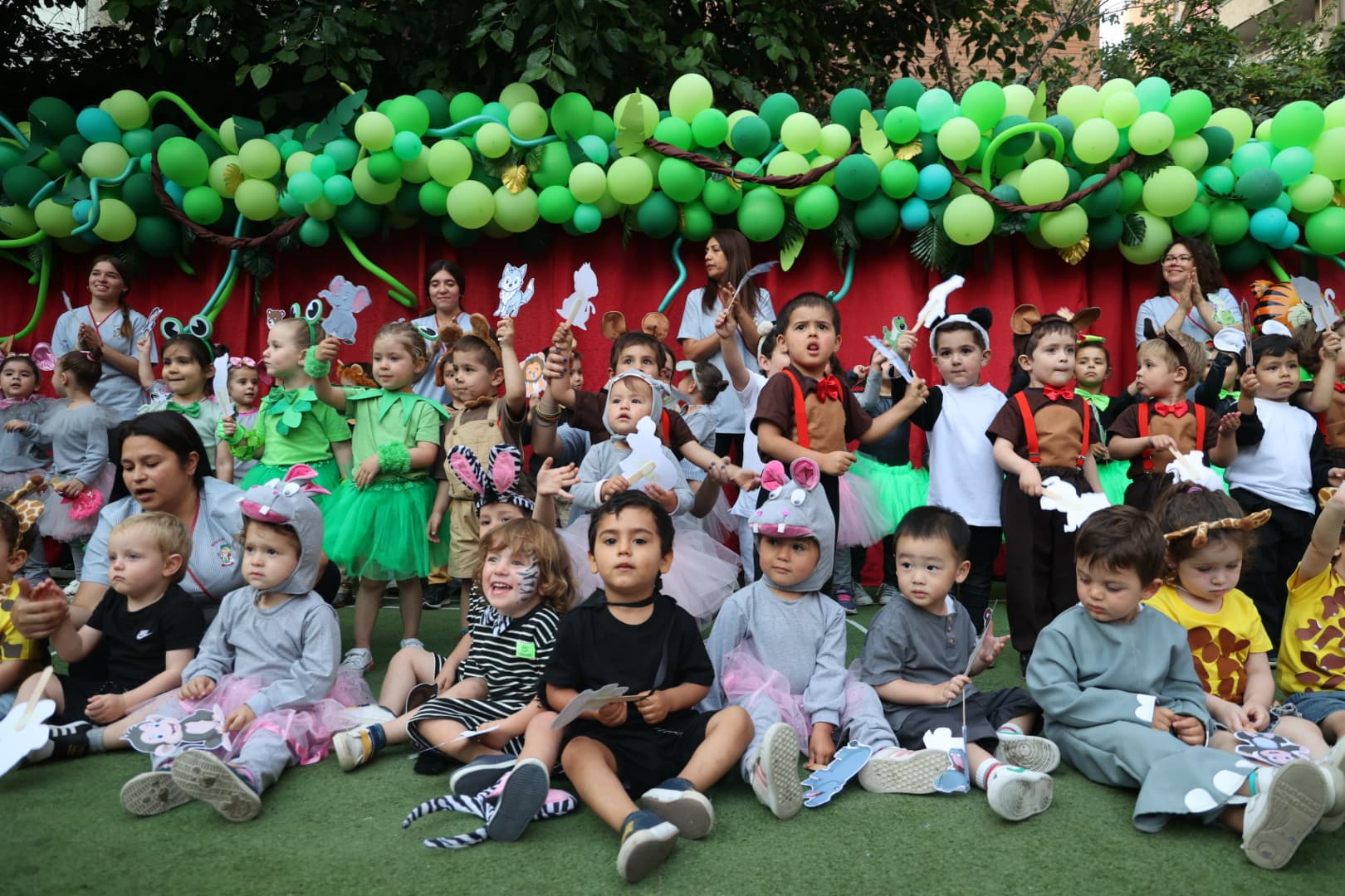 Presentación de fin de año con niños en disfraces de animales y arco de globos en el Jardín Infantil Marco Polo, Las Condes